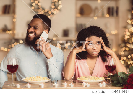 Portrait Of Annoyed Man African American Woman Is Feeling Sitting Nervous On Date In Restaurant While Her Smiling Boyfriend Talking On Smartphone, Ignoring His Girlfriend. Relationship Problem 134413495