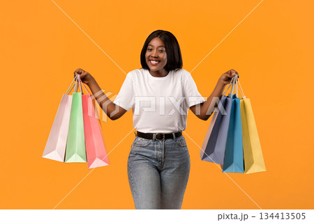 Emotional african american young woman raising hands up with colorful shopping bags and smiling, celebrating sales season beginning over orange studio background, copy space Emotional african american young woman raising hands up with colorful shopping bags and smiling, celebrating sales season beginning over orange studio background, copy space 134413505