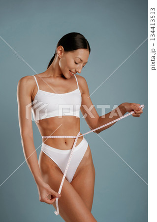 Measuring the waist, diet concept. Young woman is in the studio against background Measuring the waist, diet concept. Young woman is in the studio against background 134413513