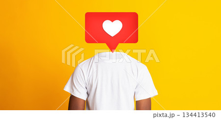 A person stands with their back turned, wearing a white t-shirt against a bright yellow background. A red heart icon appears instead of their head, symbolizing social media interactions. 134413540