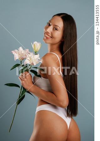 Showing body and holding flowers. Young woman is in the studio against background 134413555
