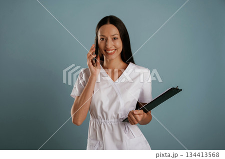 In professional lab coat, nurse is standing. Young woman is in the studio against background 134413568