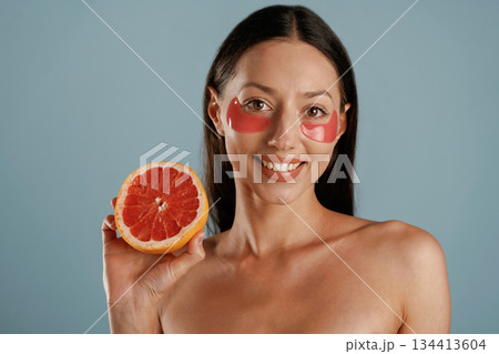 Red patches under eyes, holding grapefruit. Young woman is in the studio against background Red patches under eyes, holding grapefruit. Young woman is in the studio against background 134413604