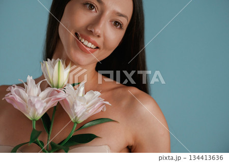 Posing with lily flower. Young woman is in the studio against background Posing with lily flower. Young woman is in the studio against background 134413636