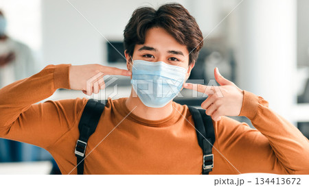 Protection Concept. Portrait of asian guy wearing medical surgical face mask to prevent infection, illness, flu or covid-19, pointing at his covered mouth standing in classroom at university. Pandemic 134413672