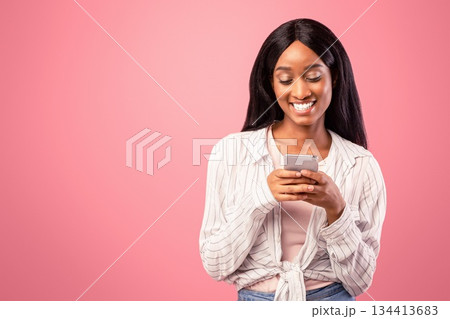 Pretty young black woman surfing web on smartphone on pink studio background. African American lady using mobile device for online studies or work, communicating with friends on internet 134413683