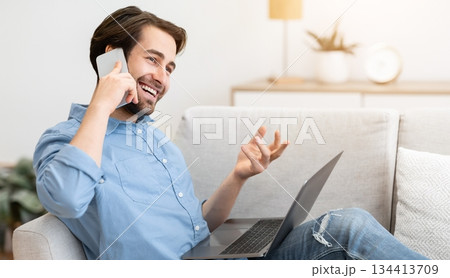 Cheerful Guy Talking On Phone Sitting With Laptop Computer On Sofa At Home. Modern Communication And Lifestyle. Happy Man Chatting On Cellphone And Laughing Indoors Cheerful Guy Talking On Phone Sitting With Laptop Computer On Sofa At Home. Modern Communication And Lifestyle. Happy Man Chatting On Cellphone And Laughing Indoors 134413709