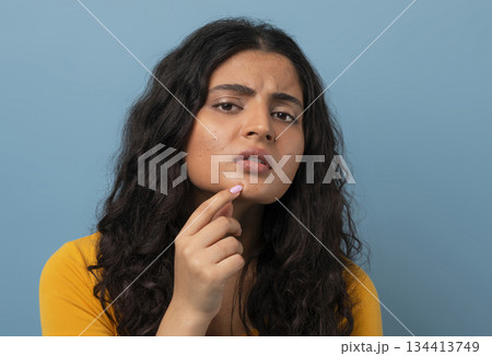 Stressed sad brunette young indian woman touching her face over blue studio background, having skin problems, closeup. Acne, pimples, wrinkles, dull skin Stressed sad brunette young indian woman touching her face over blue studio background, having skin problems, closeup. Acne, pimples, wrinkles, dull skin 134413749
