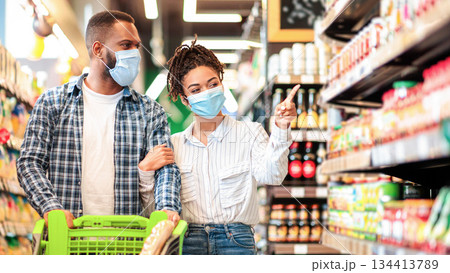African American Couple In Protective Masks In Supermarket Doing Grocery Shopping, Buying Food Essentials Walking With Shop Cart In Groceries Store Indoors. Family Choosing Food Products On Shelves African American Couple In Protective Masks In Supermarket Doing Grocery Shopping, Buying Food Essentials Walking With Shop Cart In Groceries Store Indoors. Family Choosing Food Products On Shelves 134413789