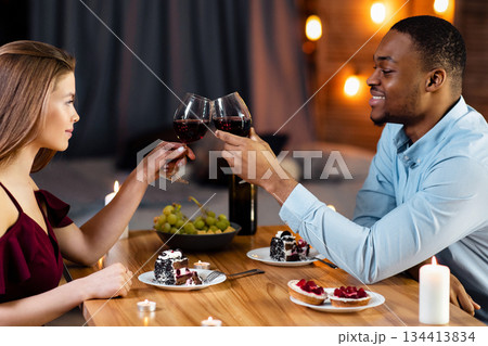 Happy Black Man And White Woman Having Romantic Dinner In Restaurant, Dating Interracial Couple Clinking Glasses With Wine And Enjoying Desserts, Celebrating Valentine's Day Together, Side View 134413834