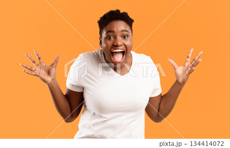 Joyful Plus-Size African Woman Screaming In Excitement Holding Hands Near Face Posing Looking At Camera On Yellow Background In Studio. Positive Emotion, Omg, Unexpected Joyful Surprise Concept Joyful Plus-Size African Woman Screaming In Excitement Holding Hands Near Face Posing Looking At Camera On Yellow Background In Studio. Positive Emotion, Omg, Unexpected Joyful Surprise Concept 134414072