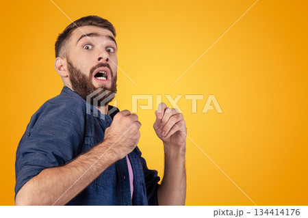 Young hipster guy being scared or terrified over grey studio background. Millennial man suffering from fear or shock, having panic attack. Negative human emotions and feelings concept Young hipster guy being scared or terrified over grey studio background. Millennial man suffering from fear or shock, having panic attack. Negative human emotions and feelings concept 134414176