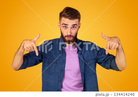 Surprised bearded guy pointing downwards on orange studio background, panorama. Emotional Caucasian guy showing or advertising something, offering big sale or product promotion Surprised bearded guy pointing downwards on orange studio background, panorama. Emotional Caucasian guy showing or advertising something, offering big sale or product promotion 134414240