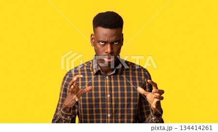 Portrait of annoyed black guy in checkered shirt emotionally gesturing, raising hands and rolling eyes with rage, feeling angry and stressed while standing isolated over yellow background, copy space 134414261