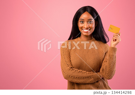 Young black woman with credit card looking at camera and smiling over pink studio background. Portrait of African American lady feeling satisfied with bank services, using contactless payment Young black woman with credit card looking at camera and smiling over pink studio background. Portrait of African American lady feeling satisfied with bank services, using contactless payment 134414298