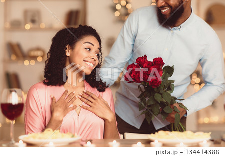 African american bearded young guy presenting bouquet of flowers to his excited girlfriend, making her surprise on a special date. Loving couple celebrating Valentine's Day, birthday or anniversary African american bearded young guy presenting bouquet of flowers to his excited girlfriend, making her surprise on a special date. Loving couple celebrating Valentine's Day, birthday or anniversary 134414388