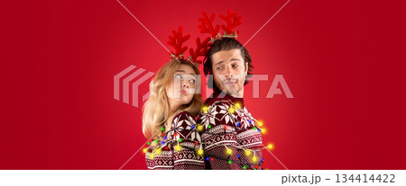 Young man and his girlfriend tied together with Christmas lights over red background 134414422