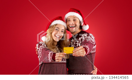 Shopping for Christmas. Smiling young couple showing contactless credit card over red background Shopping for Christmas. Smiling young couple showing contactless credit card over red background 134414565