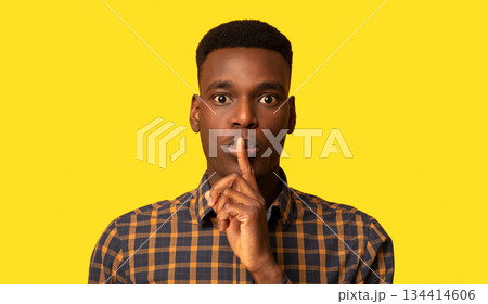 It's A Secret. Young Black Guy Making Shh Silence Gesture, Mysterious African Man Putting Finger On Lips And Looking At Camera While Standing Isolated Over Yellow Background, Closeup Shot, Copy Space 134414606