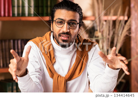 Arab Teacher Man Talking To Camera Teaching Online Explaining Lecture To Remote Students Sitting In Living Room Near Books Shelf Indoor, Working From Home. E-Teaching, Remote Tutoring. Selective Focus 134414645
