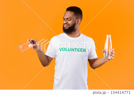 No More Plastic. African Volunteer Guy Choosing Between Glass And Plastic Bottle Standing Over Yellow Studio Background. Ecology And Environment Concept No More Plastic. African Volunteer Guy Choosing Between Glass And Plastic Bottle Standing Over Yellow Studio Background. Ecology And Environment Concept 134414771