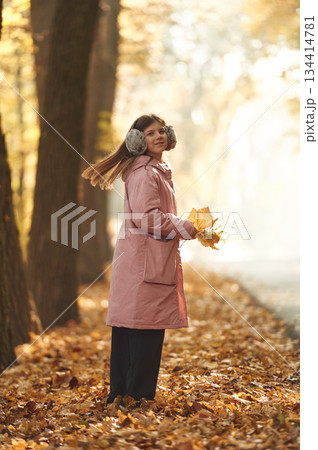 Girl in warm headphones is in the autumn forest, holding fallen leaves 134414781