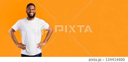 Happy African American Man Standing With His Hands On Hips Posing Near Empty Space For Text On Yellow Studio Background, Smiling To Camera. Advertisement Banner Concept. Panorama 134414800