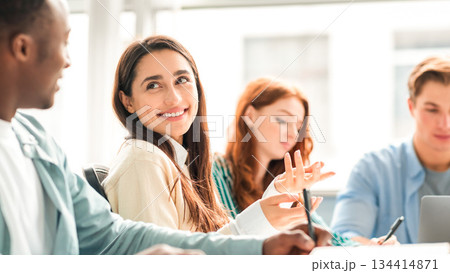 Positive Social Interaction. Cheerful friends or colleagues enjoying working process and cooperation, writing in notebooks and talking, sharing ideas preparing doing group project in college library 134414871