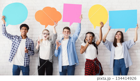 Speech bubbles. Happy friends holding empty placards over white brick wall 134414926