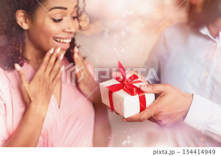 Closeup of excited surprised young african american woman receiving gift from her boyfriend. Affectionate millennial couple celebrating Valentine's Day, making surprise for birthday or anniversary Closeup of excited surprised young african american woman receiving gift from her boyfriend. Affectionate millennial couple celebrating Valentine's Day, making surprise for birthday or anniversary 134414949