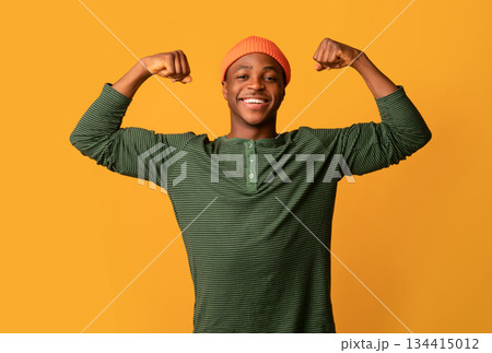 Strong Black Hipster Guy In Orange Hat Showing Biceps Muscles And Looking At Camera, Positive Confident Young African American Man Demonstrating His Strength, Posing On Yellow Background, Copy Space Strong Black Hipster Guy In Orange Hat Showing Biceps Muscles And Looking At Camera, Positive Confident Young African American Man Demonstrating His Strength, Posing On Yellow Background, Copy Space 134415012