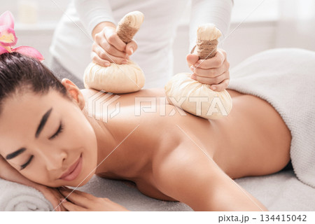 Relaxed asian woman having herbal ball compress back and shoulder massage session in spa salon, calm korean lady enjoying body treatments and self-pampering herself with beauty procedures, closeup Relaxed asian woman having herbal ball compress back and shoulder massage session in spa salon, calm korean lady enjoying body treatments and self-pampering herself with beauty procedures, closeup 134415042