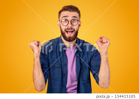Winner and success concept. Excited young guy making YES gesture with clenched fists on orange studio background. Excited Caucasian man shouting OMG, overjoyed with big win 134415105