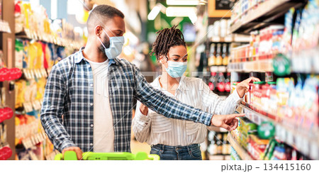 African Husband And Wife In Protective Face Masks Shopping Groceries In Supermarket Buying Food Essentials Walking With Shop Trolley Cart In Grocery Store Indoor. Family Preparing For Quarantine African Husband And Wife In Protective Face Masks Shopping Groceries In Supermarket Buying Food Essentials Walking With Shop Trolley Cart In Grocery Store Indoor. Family Preparing For Quarantine 134415160