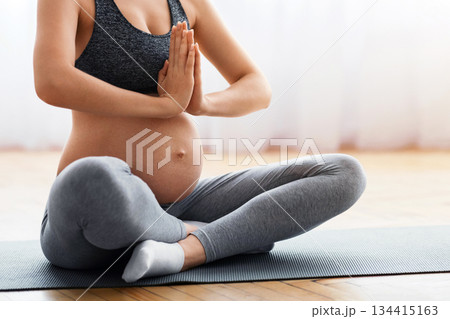 Closeup shot of unrecognizable pregnant woman meditating at home, expetcant lady sitting in lotus position with clasped hands, practicing yoga for healthy pregnancy, cropped image with free space 134415163