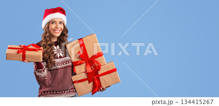 Happy young woman in Santa hat and Xmas sweater holding Christmas gifts on blue studio background, panorama. Portrait of pretty lady with wrapped presents for winter holidays looking at camera Happy young woman in Santa hat and Xmas sweater holding Christmas gifts on blue studio background, panorama. Portrait of pretty lady with wrapped presents for winter holidays looking at camera 134415267