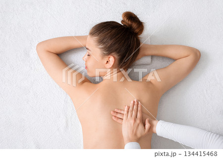 Top view of young lady having healing full body massage from unrecognizable female therapist at luxury spa. Beautiful naked woman getting relaxing back massage on white, view above Top view of young lady having healing full body massage from unrecognizable female therapist at luxury spa. Beautiful naked woman getting relaxing back massage on white, view above 134415468