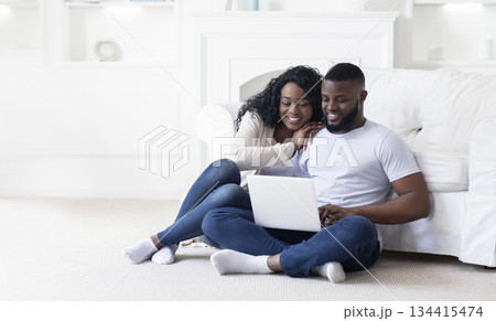 Planning summer vacation. Happy african american spouses using laptop booking hotel online, while sitting on floor at home, panorama with free space Planning summer vacation. Happy african american spouses using laptop booking hotel online, while sitting on floor at home, panorama with free space 134415474