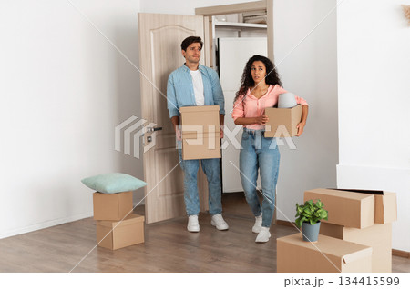 Unhappy confused millennial couple homeowners holding cardboard boxes walking in new house, young family of two people moving into bad flat, sad guy and lady disappointed in interior design 134415599