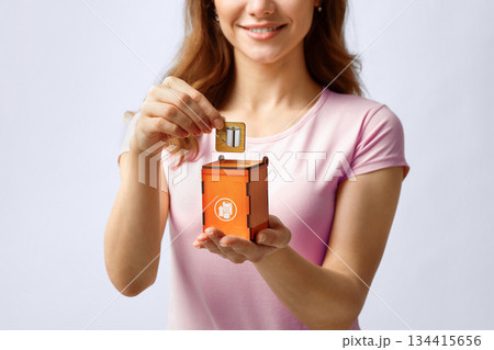 Metal Waste Utilization. Unrecognizable Woman Putting Card With Drawn Iron Mug Into Wooden Toy Trash Container, Standing Over Gray Studio Background, Conceptual Image For Waste Recycle, Copy Space Metal Waste Utilization. Unrecognizable Woman Putting Card With Drawn Iron Mug Into Wooden Toy Trash Container, Standing Over Gray Studio Background, Conceptual Image For Waste Recycle, Copy Space 134415656