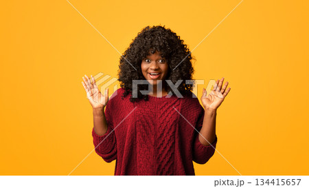 Ecstatic african american young woman smiling with hands up and wide open eyes, yellow studio background. Beautiful black lady expressing strong positive emotions, screaming and gesturing 134415657
