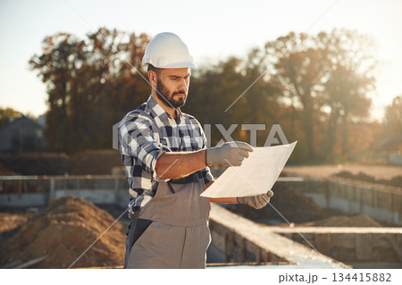 Holding plan in hands. Worker is on the construction site at daytime 134415882