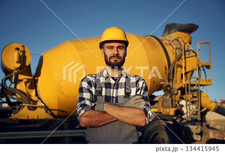 Against concrete mixer truck. Worker is on the construction site at daytime Against concrete mixer truck. Worker is on the construction site at daytime 134415945