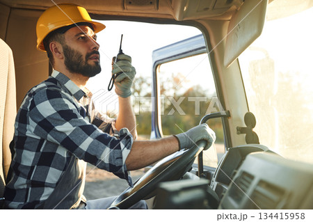 Holding radio, walkie talkie. Construction worker is sitting in the truck cabin 134415958