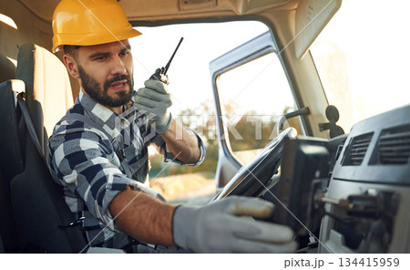 Holding radio, walkie talkie. Construction worker is sitting in the truck cabin Holding radio, walkie talkie. Construction worker is sitting in the truck cabin 134415959