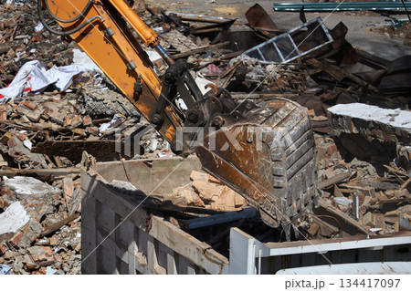 Excavator bucket loading debris into a dump truck, illustrating demolition, construction, and waste management process on a building site. 134417097