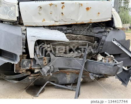 This minibus was significantly damaged as a result of a serious head-on collision. A seriously damaged grey minibus, which shows significant collision marks in the front and extensive rust marks. 134417744
