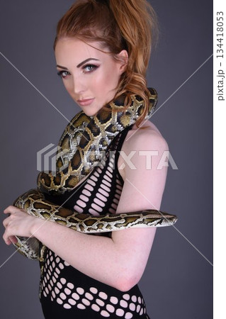 Beautiful redhead girl posing with her pet snake in the studio 134418053