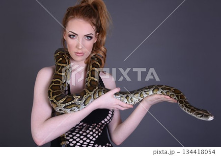 Beautiful redhead girl posing with her pet snake in the studio 134418054