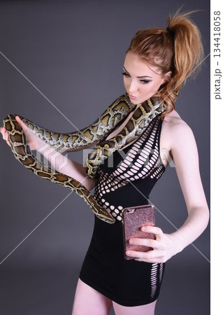 Beautiful redhead girl posing with her pet snake in the studio Beautiful redhead girl posing with her pet snake in the studio 134418058